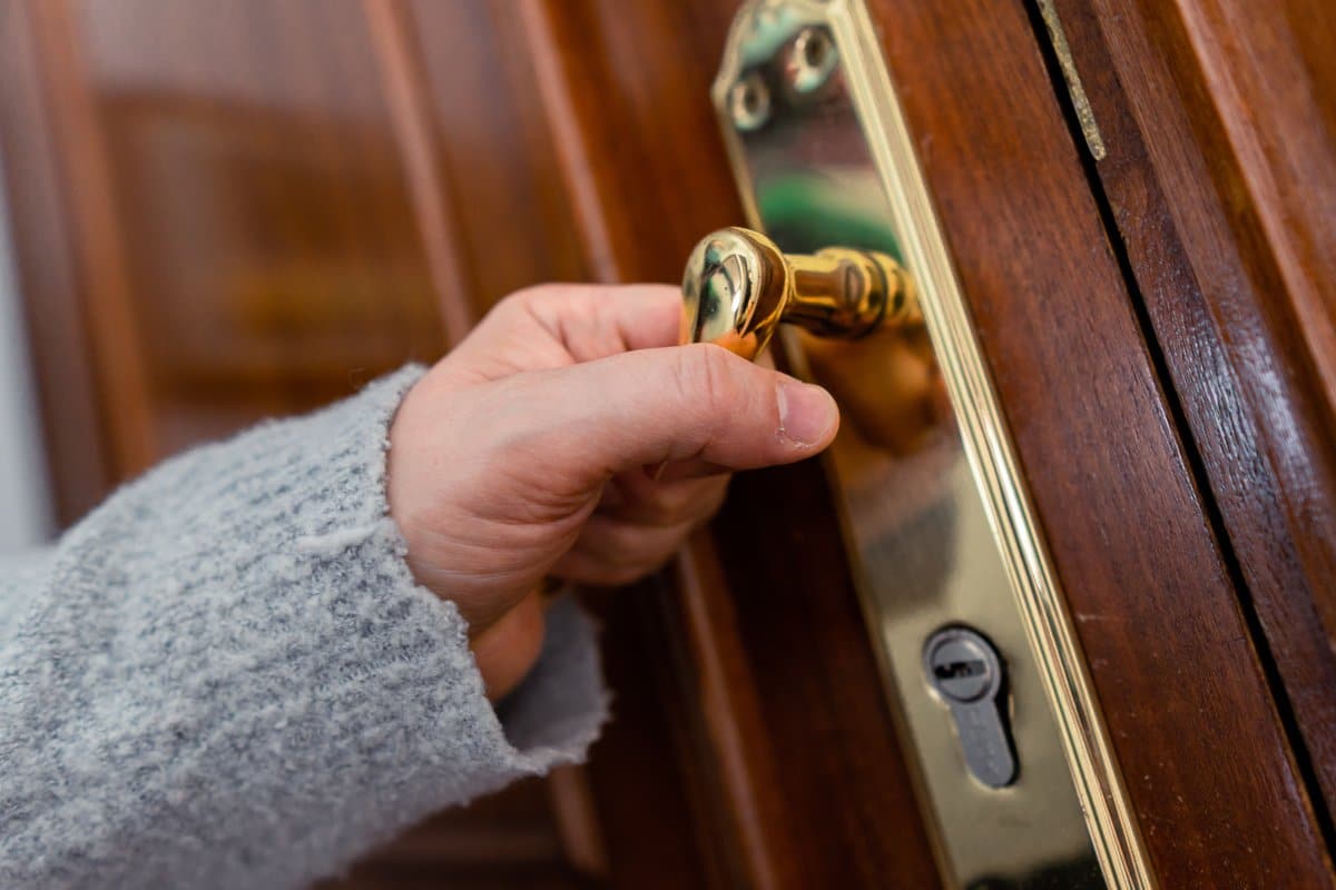 Hand draait een sleutel in een messing cilinderslot van een houten voordeur.